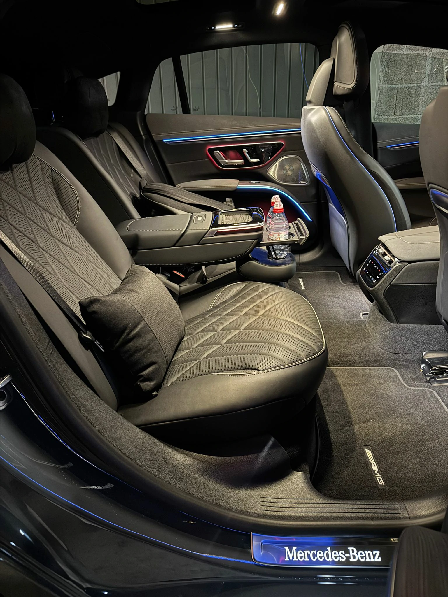 Habitacle arrière Mercedes EQS 450+ — sièges AMG, éclairage ambiance bleu, seuil Mercedes-Benz illuminé